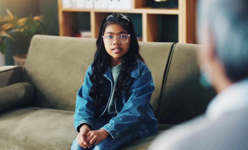 young girl is seated on a couch with her parents