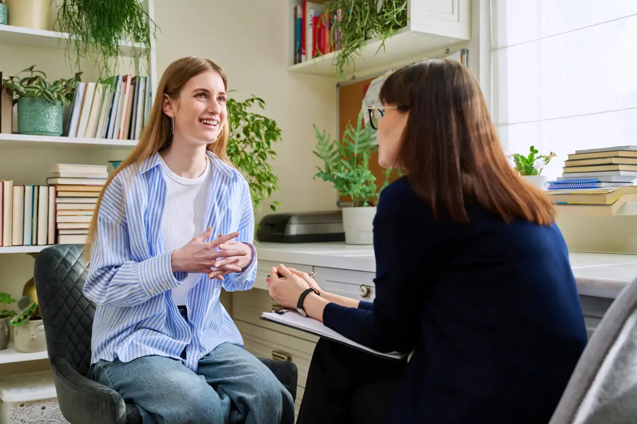woman in a chair talks animatedly to another woman standing beside her