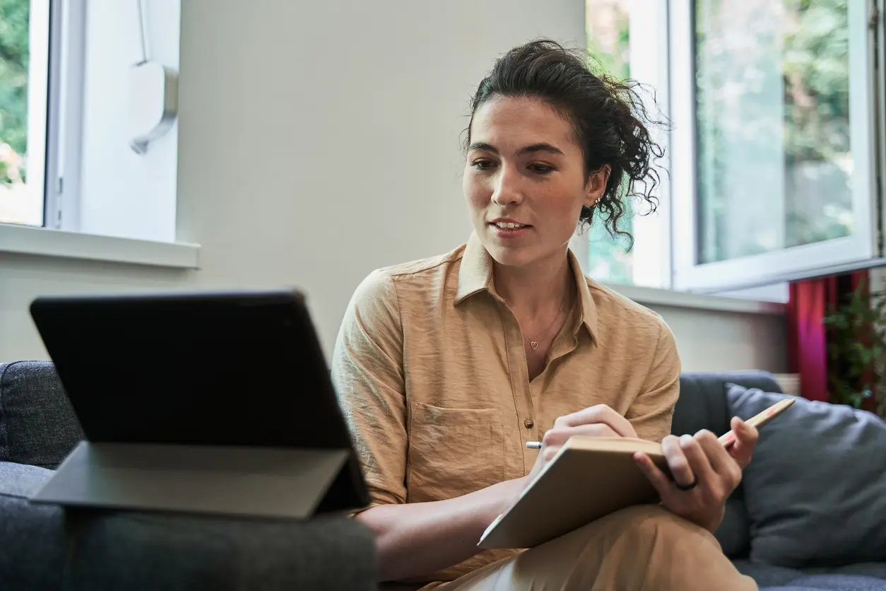 woman sitting on a couch, using a laptop and holding a pen, focused on her work