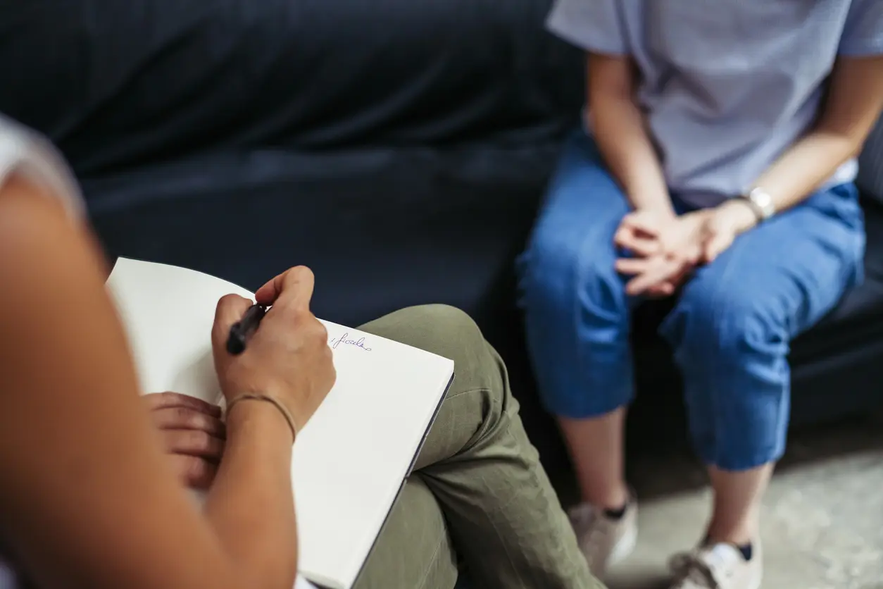 person sitting on a couch, writing in a notebook with a pen, focused on their thoughts