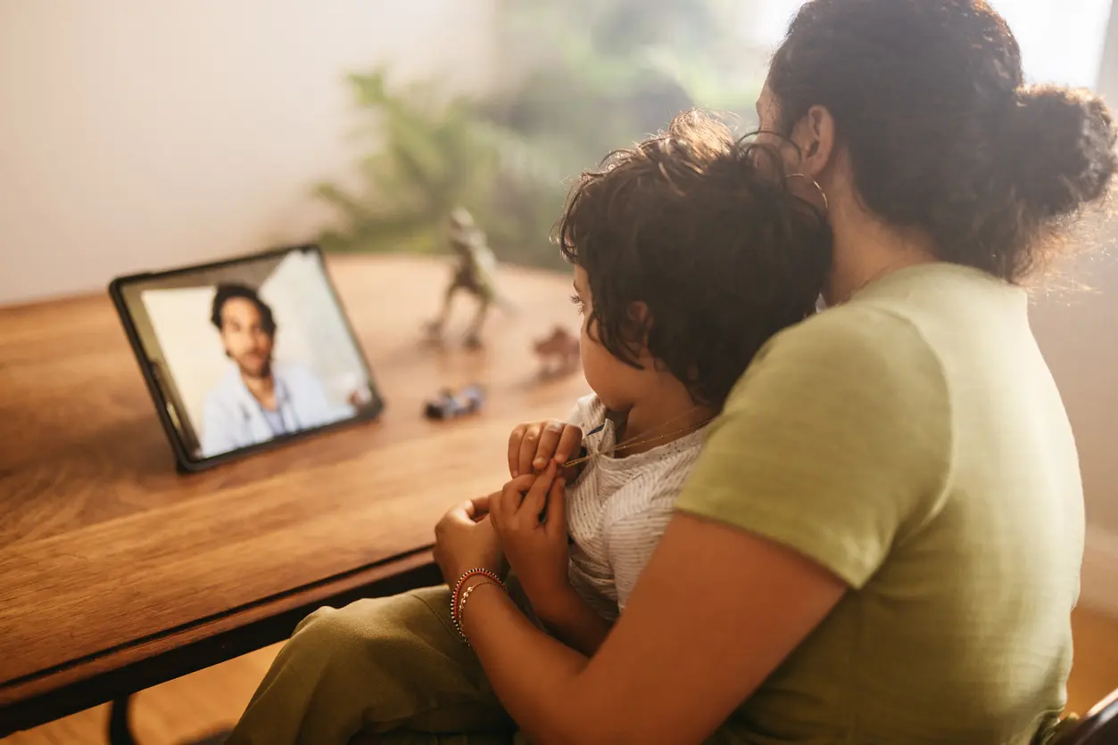 woman and a child sit together at a table, engaging with a laptop between them