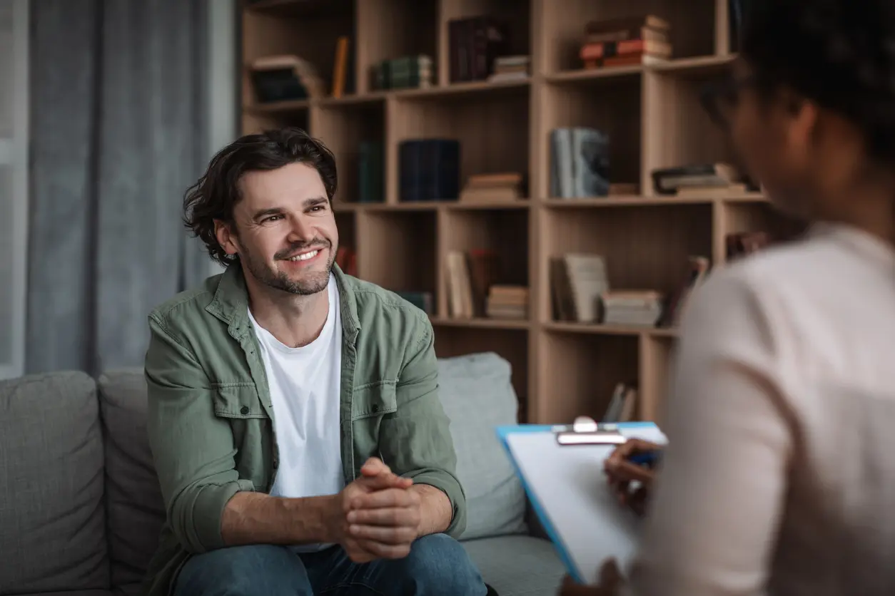 man and a woman are seated on a couch, engaged in a discussion