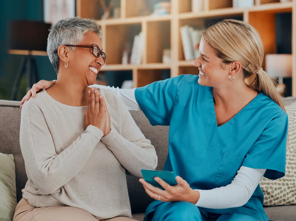 A nurse and an elderly woman are comfortably sitting on a couch caregiver and patient