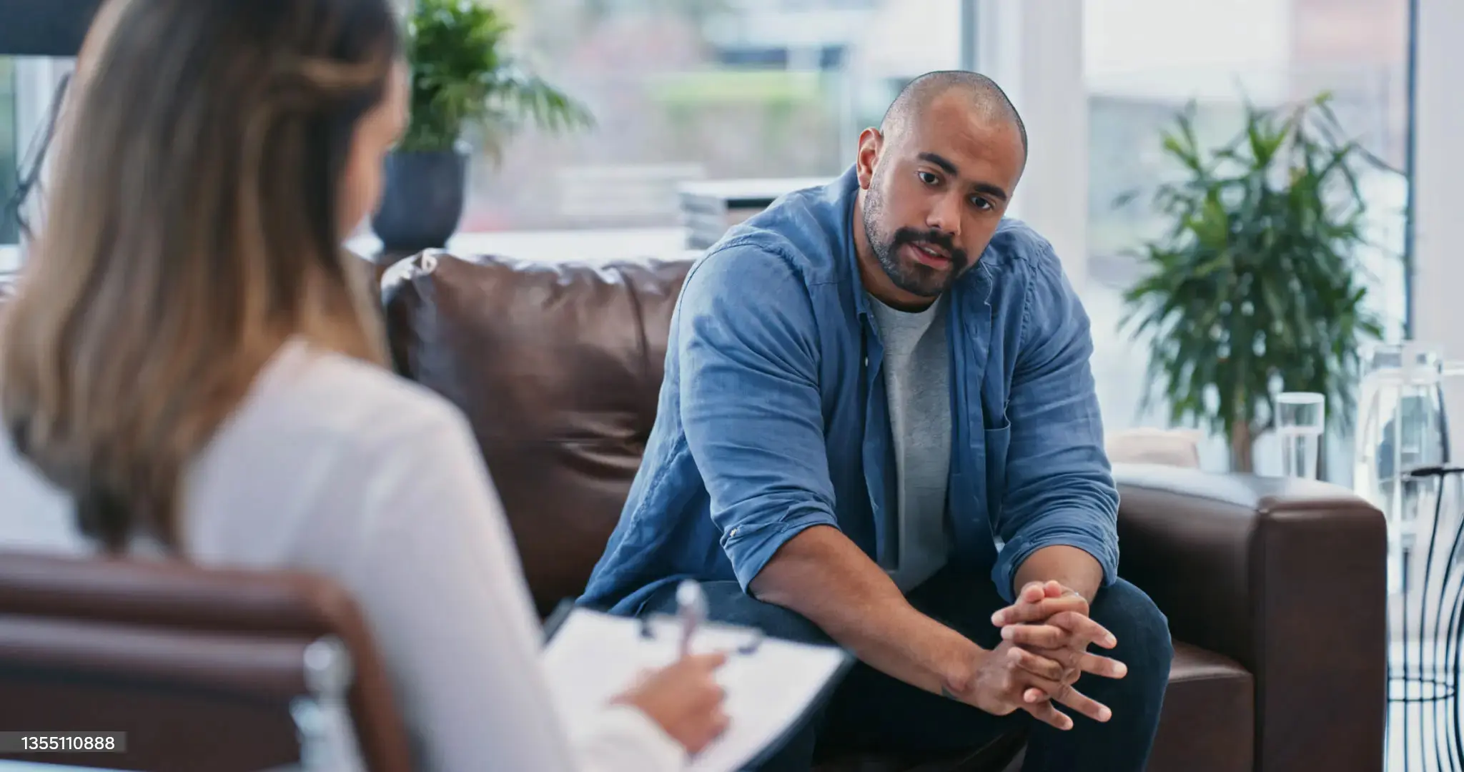 man converses with a woman while sitting together on a couch